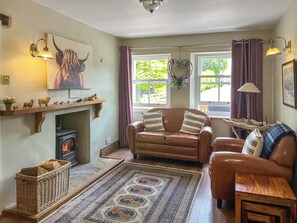 A cozy living room with a fireplace, leather sofas, a patterned rug, and a large painting of a bull. - Gillhead Farm Cottage (Matterdale End)