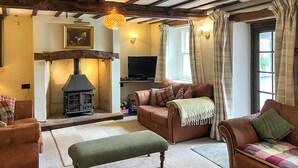 A cozy living room with a fireplace, leather sofas, a bench, and a television. - Gillhead Farm Cottage (Matterdale End)