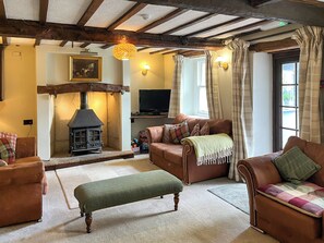 A cozy living room with a fireplace, leather sofas, a bench, and a television. - Gillhead Farm Cottage (Matterdale End)