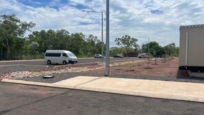 A parking area with a white van and a few cars, a concrete sidewalk, and a building in the background. - Discovery Parks Worsktay-Tindal Village (Lansdowne)