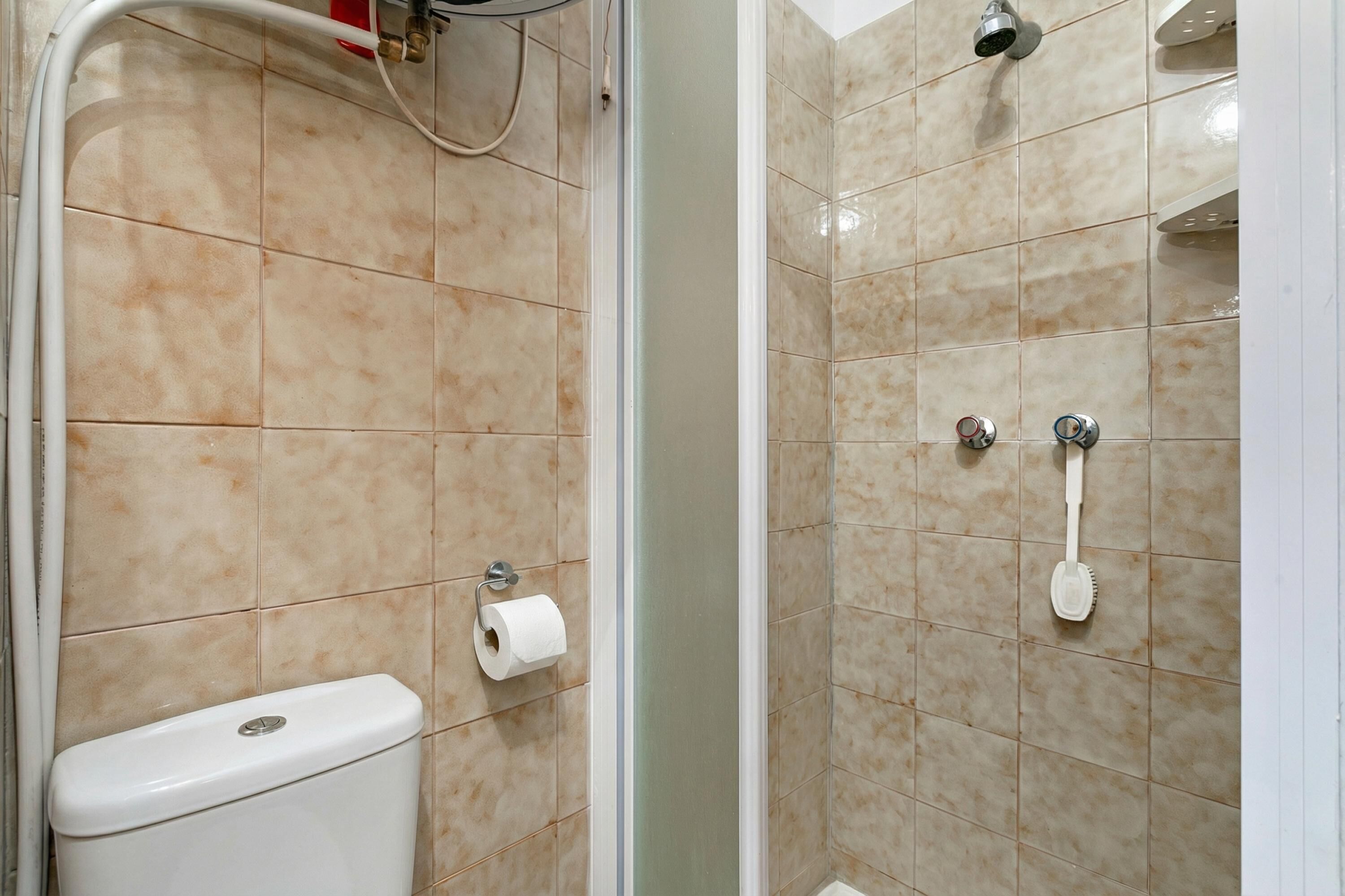 Un baño con baldosas color beige, un inodoro, una ducha con puerta de vidrio y un secador de manos.
