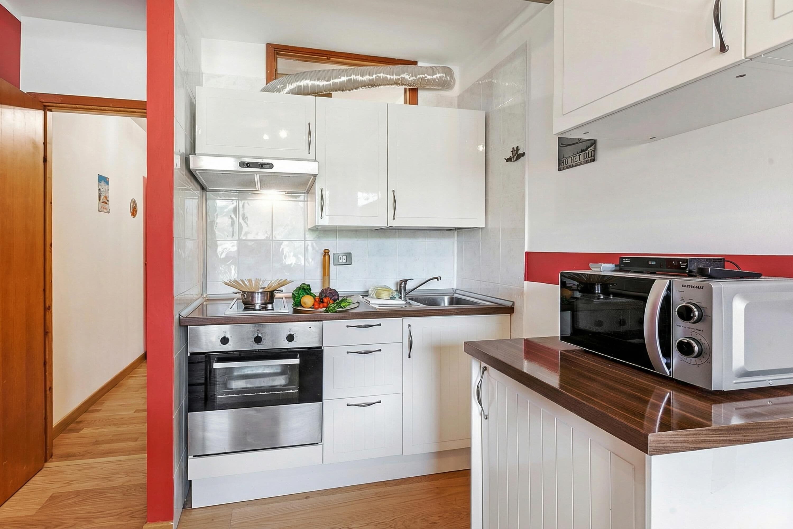 Una cocina con gabinetes blancos, microondas, estufa y fregadero.