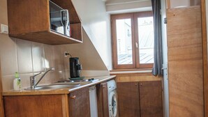 A compact kitchen with wooden cabinets, a washing machine, and a window with curtains.