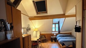 A compact, well-lit attic bedroom with a sloped ceiling, a small window, a bed, a desk, and a chair.