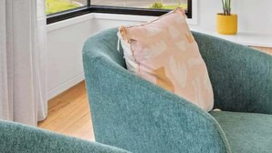 A room with a large window, a green sofa, a potted plant, and a view of a body of water. - Luxury Riverside Escape with Fire Pit, Pizza Oven, River Views (Ocean Grove)