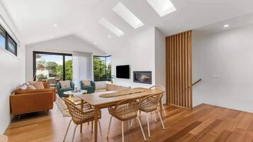 A modern living room with a wooden dining table, wicker chairs, a sofa, and a TV mounted on the wall.