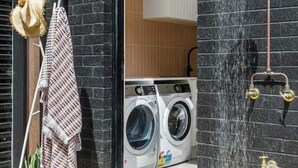 A modern building with a black brick exterior, a visible laundry area with washing machines, and a showerhead with water flowing. - Luxury Riverside Escape with Fire Pit, Pizza Oven, River Views (Ocean Grove)