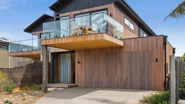 A modern two-story house with a balcony, large windows, and a wooden facade. - Luxury Riverside Escape with Fire Pit, Pizza Oven, River Views (Ocean Grove)