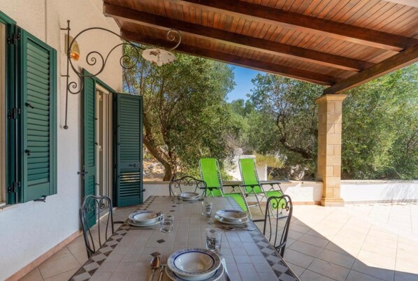 An outdoor dining area with a tiled floor, green chairs, and a table set for two.