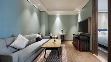 Una habitación de hotel moderna con un sofá gris, una mesa de centro de madera, un televisor y una cama.