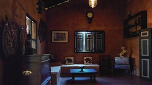 A dimly lit room with a wooden cabinet, a sofa with elephant cushions, a small table, and a decorative horse statue. - Mati Gedara Resort (Digana)