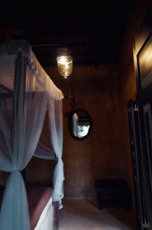 A dimly lit room with a bed under a canopy, a hanging light fixture, and a small round mirror on the wall. - Mati Gedara Resort (Digana)