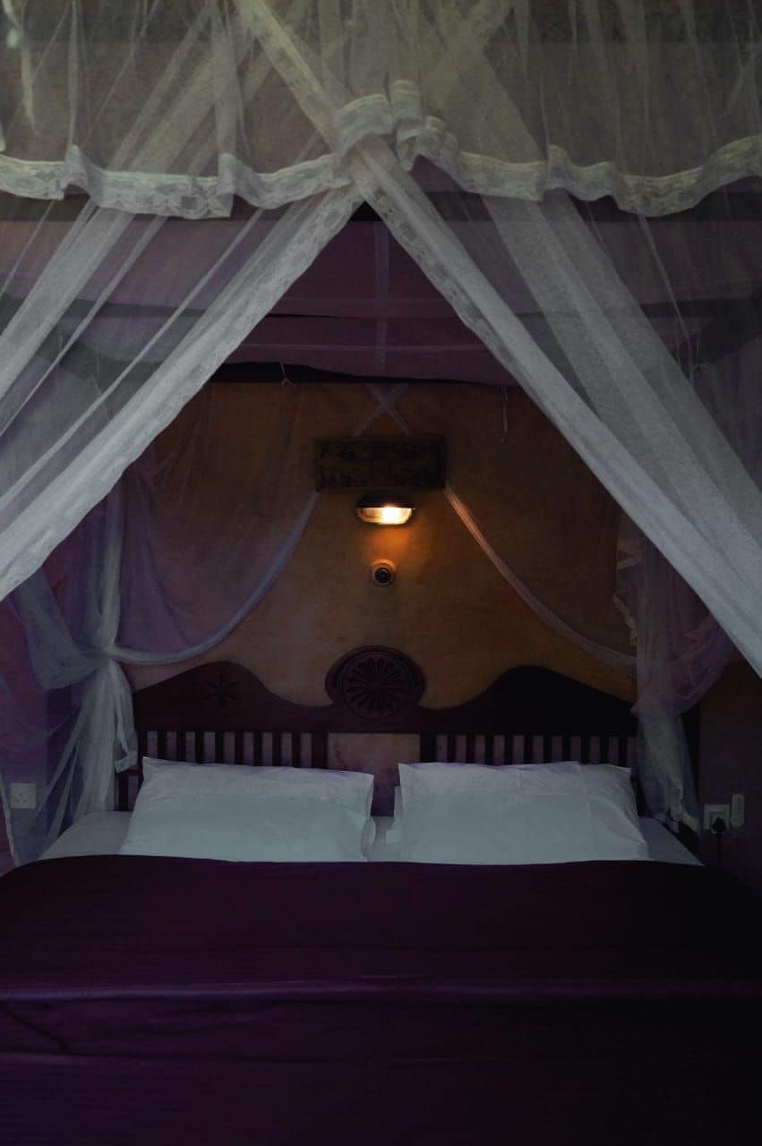 A bed with a canopy, a wall-mounted light, and a decorative wall panel.