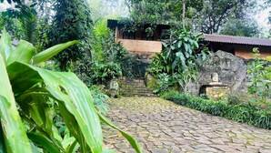 A stone-paved courtyard with lush greenery and a rustic building in the background. - Mati Gedara Resort (Digana)