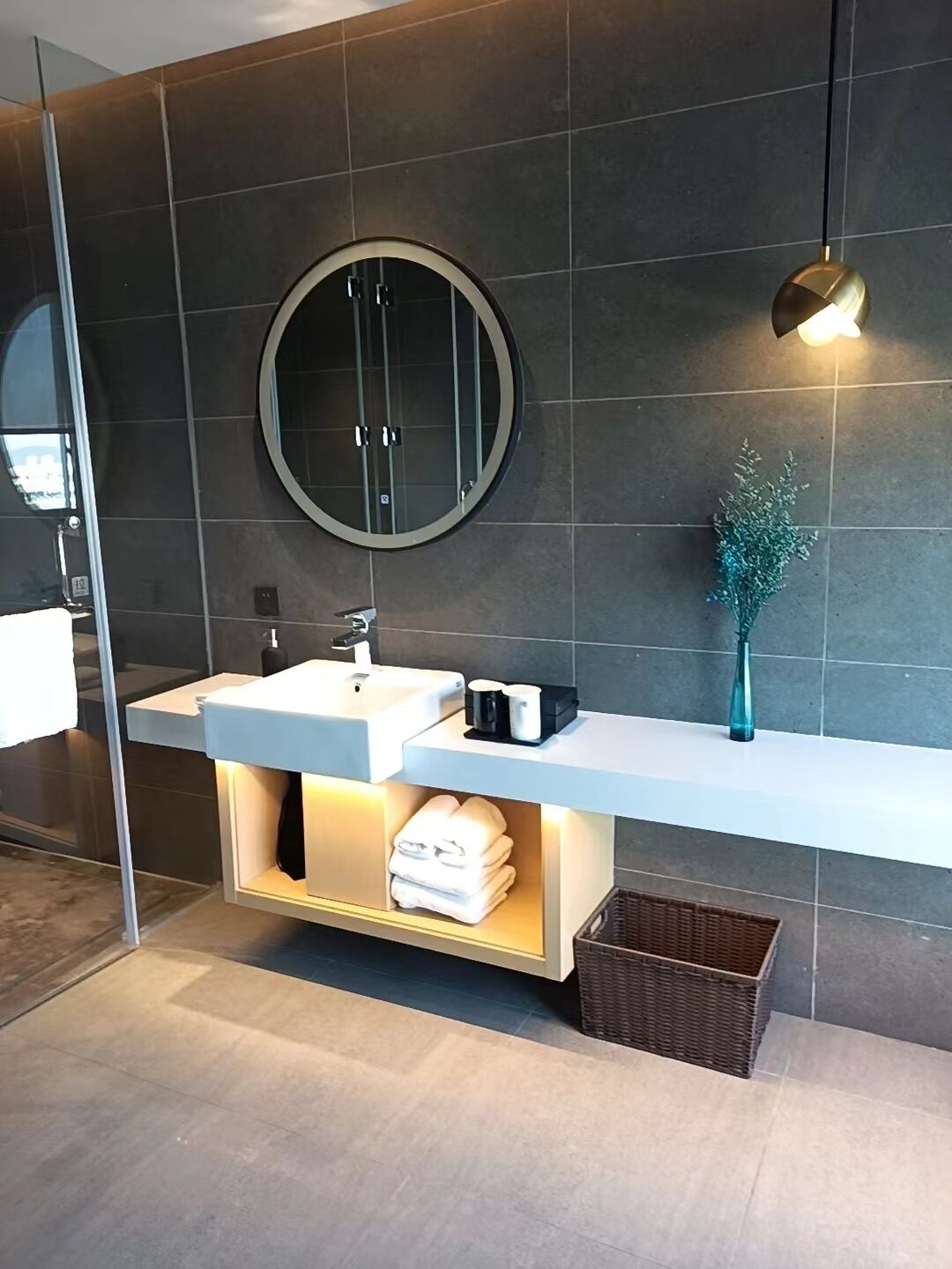 A modern bathroom with a large round mirror, a white sink, and a towel rack.