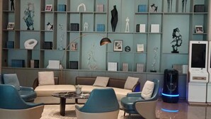 A modern living room with a sofa, armchairs, and a coffee table. There is a bookshelf with various decorative items and a ceiling light. - DeXin JunTing Hotel Wenzhou South (Wenzhou)