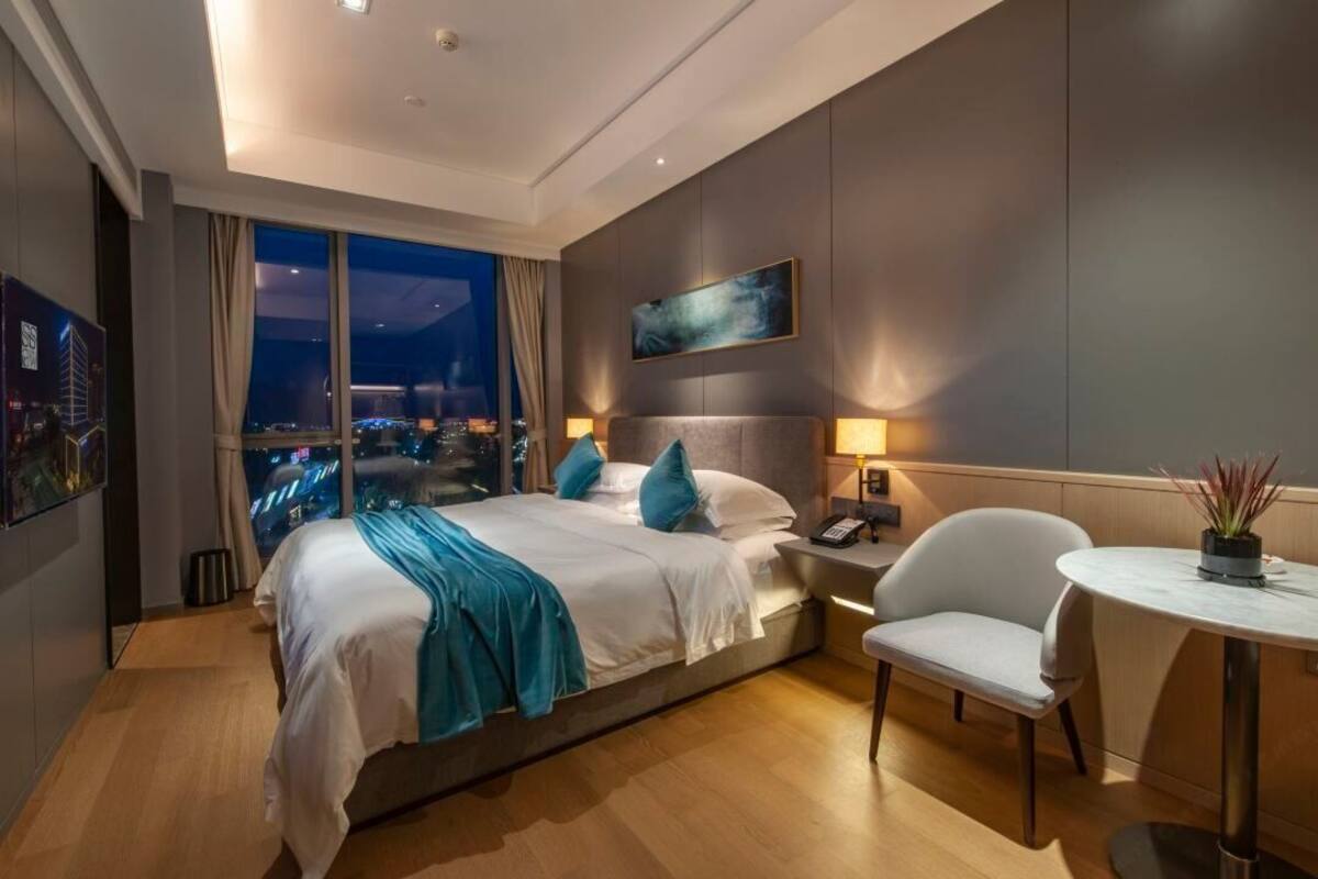 A modern hotel room with a large bed, a nightstand, a chair, and a view of the city at night.