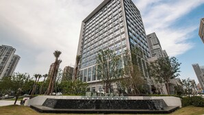 A modern high-rise hotel with a prominent entrance, surrounded by greenery and other buildings. - DeXin JunTing Hotel Wenzhou South (Wenzhou)