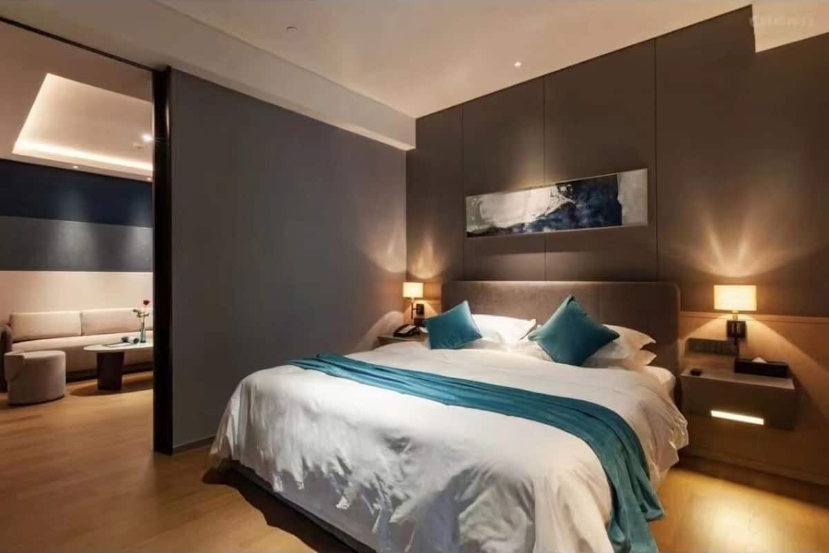 A modern hotel room with a large bed, a sofa, and a nightstand with a lamp.