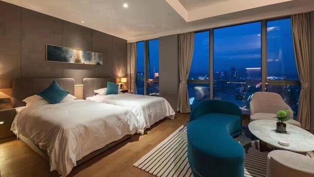 A modern hotel room with two beds, a sitting area with a round table, and a large window offering a city view. - DeXin JunTing Hotel Wenzhou South (Wenzhou)