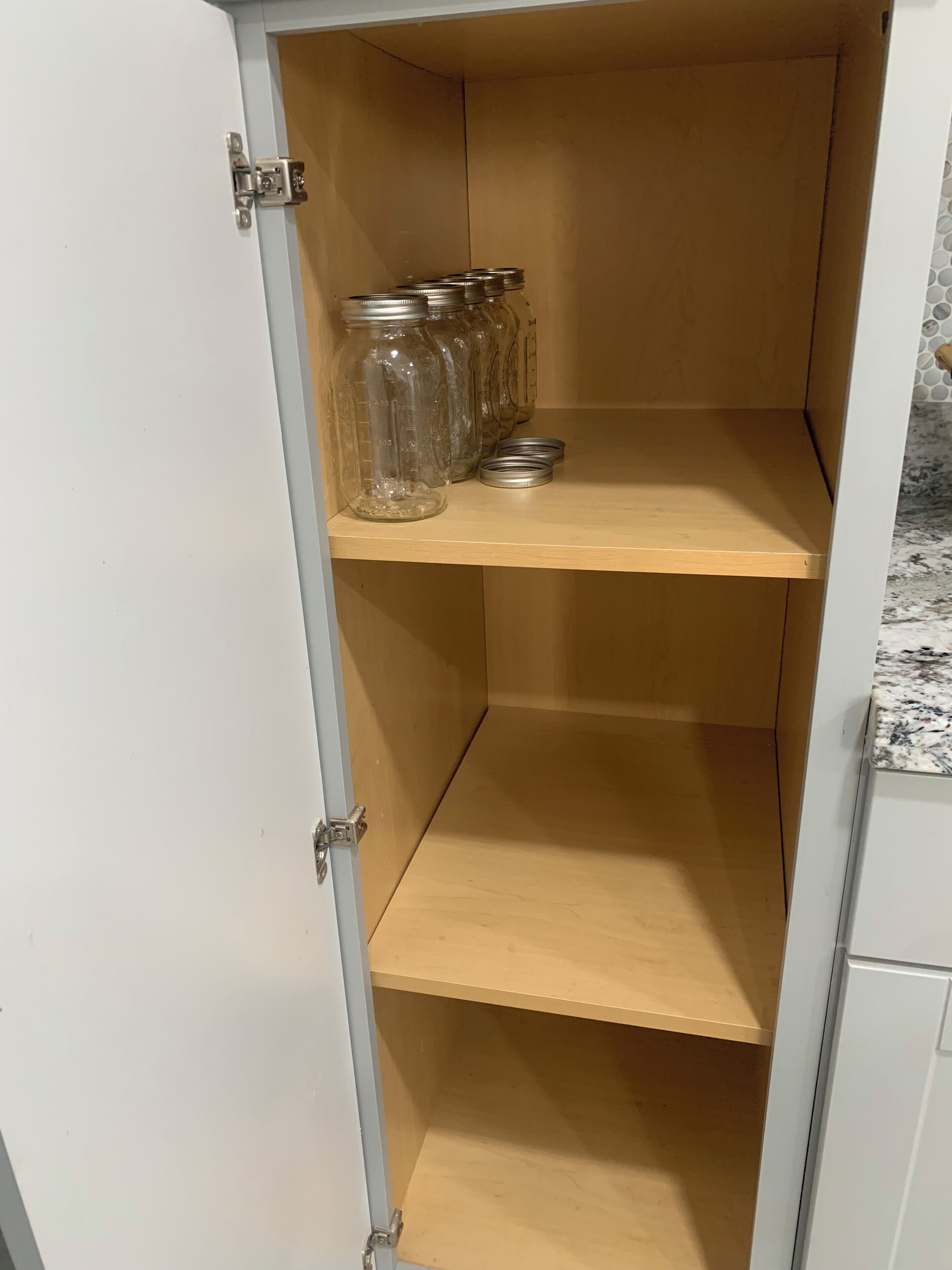 Een keukenkastje met twee planken, waarvan er één glazen potten met metalen deksels bevat.