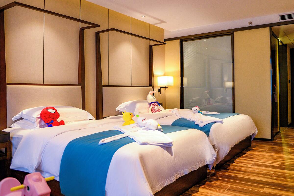 Ein Hotelzimmer mit zwei Betten, einem Nachttisch und einem großen Fenster mit Jalousien.