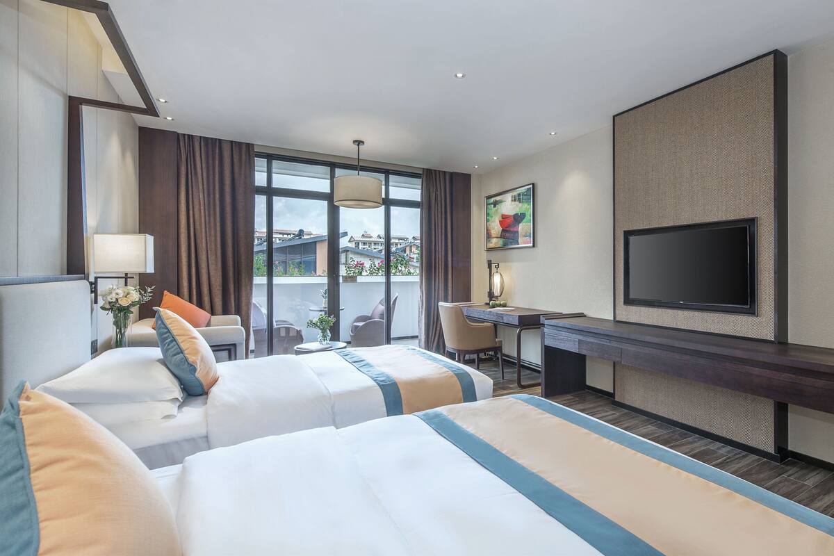 Ein Hotelzimmer mit zwei Betten, einem Schreibtisch, einem Fernseher und einem großen Fenster mit Blick auf die Stadt.