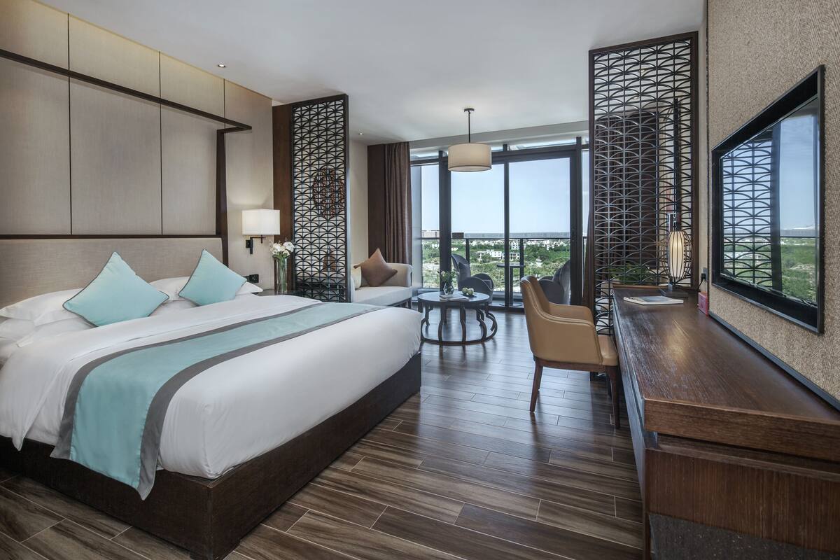 Ein modernes Hotelzimmer mit einem großen Bett, einem Schreibtisch, einem runden Tisch und Blick auf die Stadt.