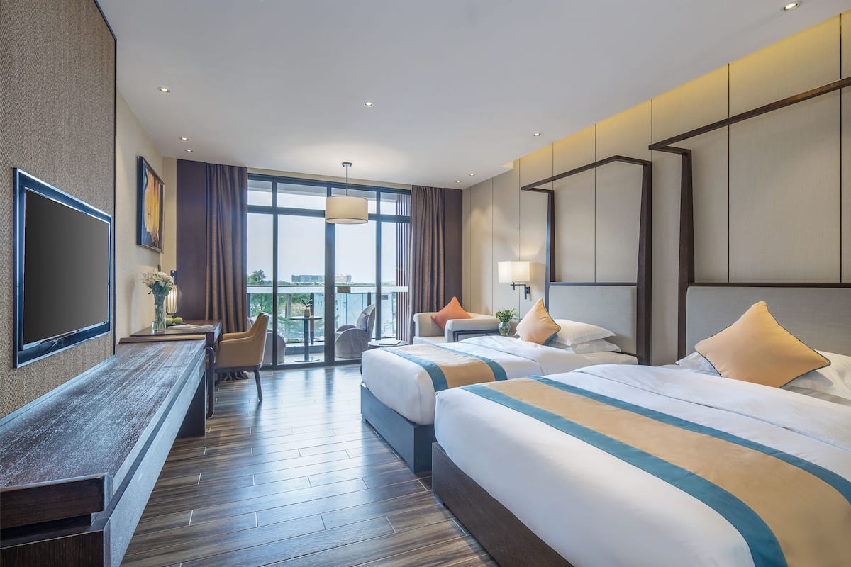 Ein Hotelzimmer mit zwei Betten, einem Fernseher, einem Schreibtisch und einem Balkon mit Blick.