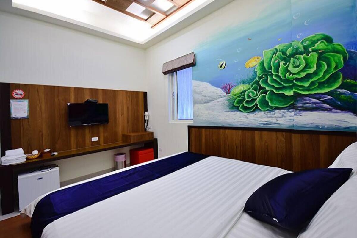 Habitación de hotel con una cama, un televisor montado en la pared, una ventana y un mural con una escena submarina.