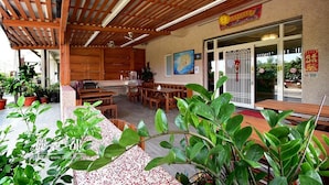 An outdoor patio area with wooden furniture, potted plants, and a large painting on the wall.