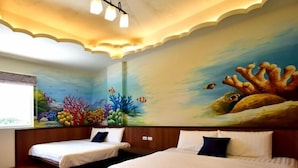 A hotel room with two beds, a mural of an underwater scene on the wall, and a window with a view of the sea.