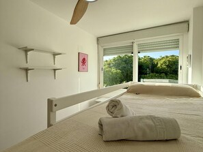 Ein Schlafzimmer mit einem Bett, einem Handtuch, einem Bilderrahmen und einem Fenster mit Blick auf Grünfläche.