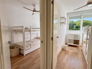Una habitación con literas, ventilador de techo, ventana con vistas y un pequeño escritorio.