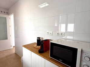 Eine Küche mit weißen Fliesen, einer Mikrowelle, einem roten Toaster und einer Kaffeemaschine auf der Arbeitsplatte.