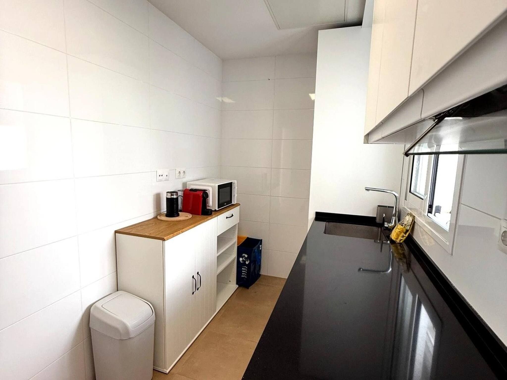 A modern kitchen with white cabinetry, a black countertop, and a stainless steel sink.