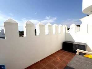 A rooftop terrace with a white wall, a tiled floor, and a small seating area.