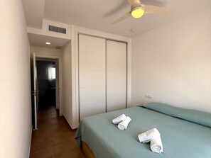 A hotel room with a bed, a ceiling fan, and a door leading to another room.