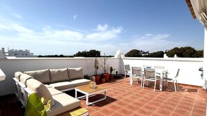Eine Dachterrasse mit einer Couch, einem Tisch, Stühlen und Blumentöpfen.
