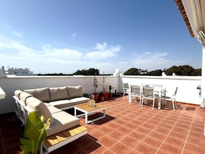 Eine Dachterrasse mit einer Couch, einem Tisch, Stühlen und Blumentöpfen.