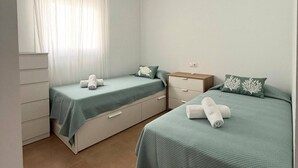 Ein Schlafzimmer mit zwei Betten, einem Deckenventilator, einem Fenster mit Vorhängen und einem Nachttisch mit Lampe.