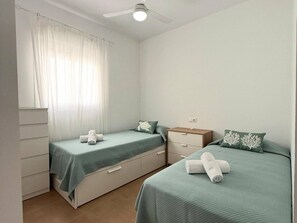 Ein Schlafzimmer mit zwei Betten, einem Deckenventilator, einem Fenster mit Vorhängen und einem Nachttisch mit Lampe.