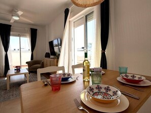 A dining area with a table set for two, a bottle of wine, and a television in the background.