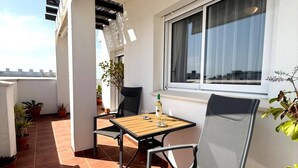 Ein Balkon mit Tisch und Stühlen, Blumentöpfen und einem Fenster mit Vorhängen.