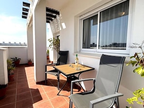 Ein Balkon mit Tisch und Stühlen, Blumentöpfen und einem Fenster mit Vorhängen.