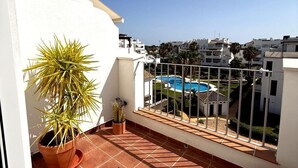 A balcony with a potted plant, a view of a swimming pool, and surrounding buildings.