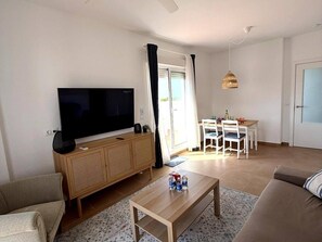Ein Wohnzimmer mit Flachbildfernseher, Holzschrank, Sofa, Couchtisch und einem Essbereich mit Stühlen und Tisch.