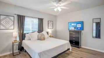 Habitación de hotel con cama, ventilador de techo, televisor y cómoda.