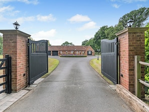 A gated driveway leading to a brick building with a garage and a small garden. - The Pool House - UK49372 (Woking, near Guildford)