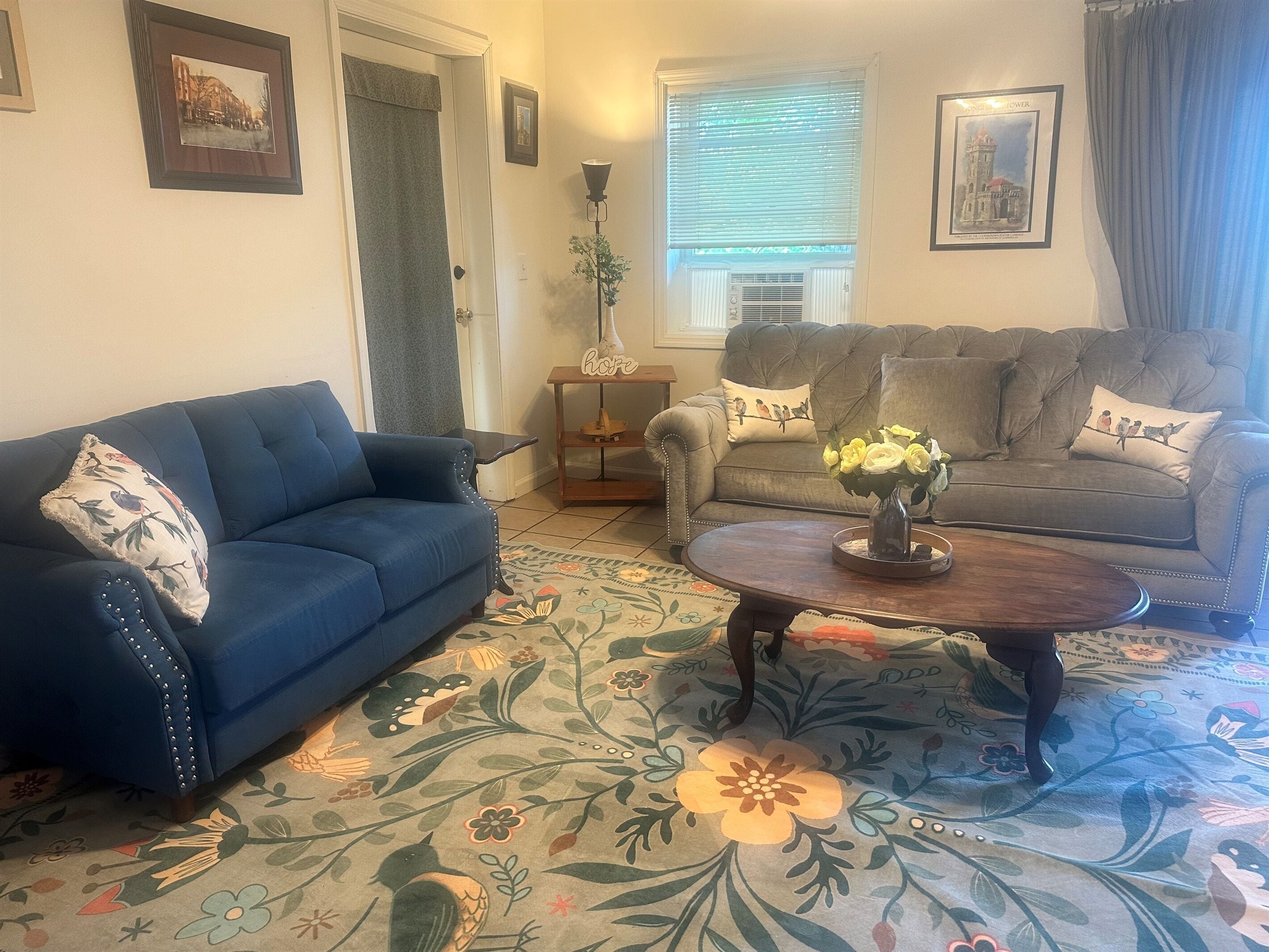 A living room with a blue sofa, a grey sofa, a coffee table with flowers, and a patterned rug.